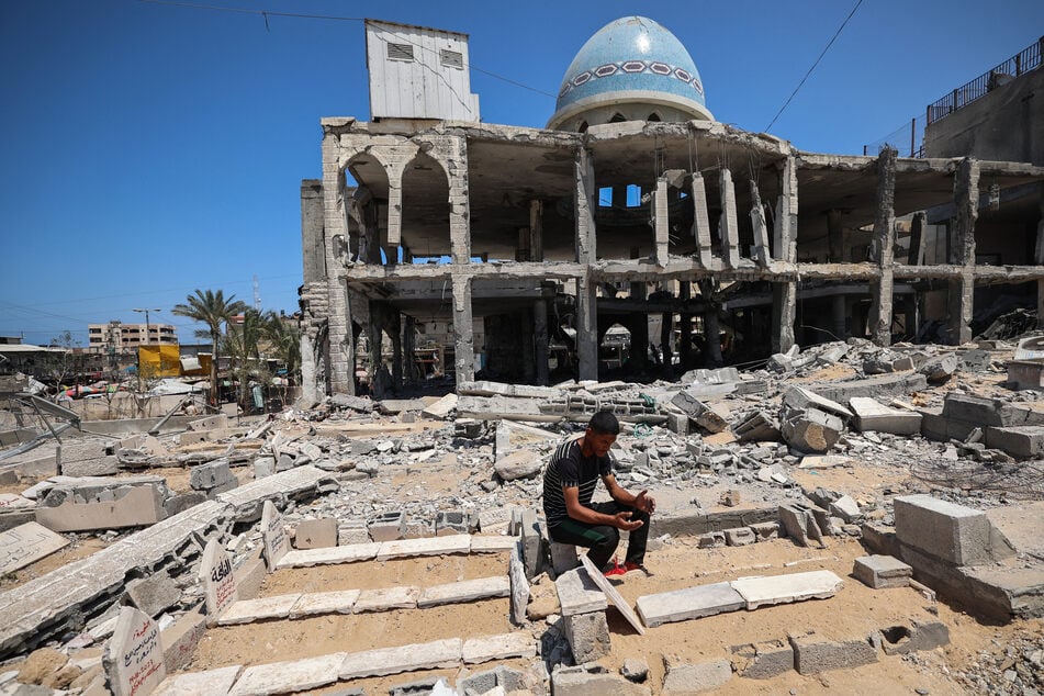 A Palestinian man recites the Fatiha over a damaged grave after an Israeli strike that hit the Ansar Mosque and the adjacent cemetery in Deir el-Balah in the central Gaza Strip on Tuesday.