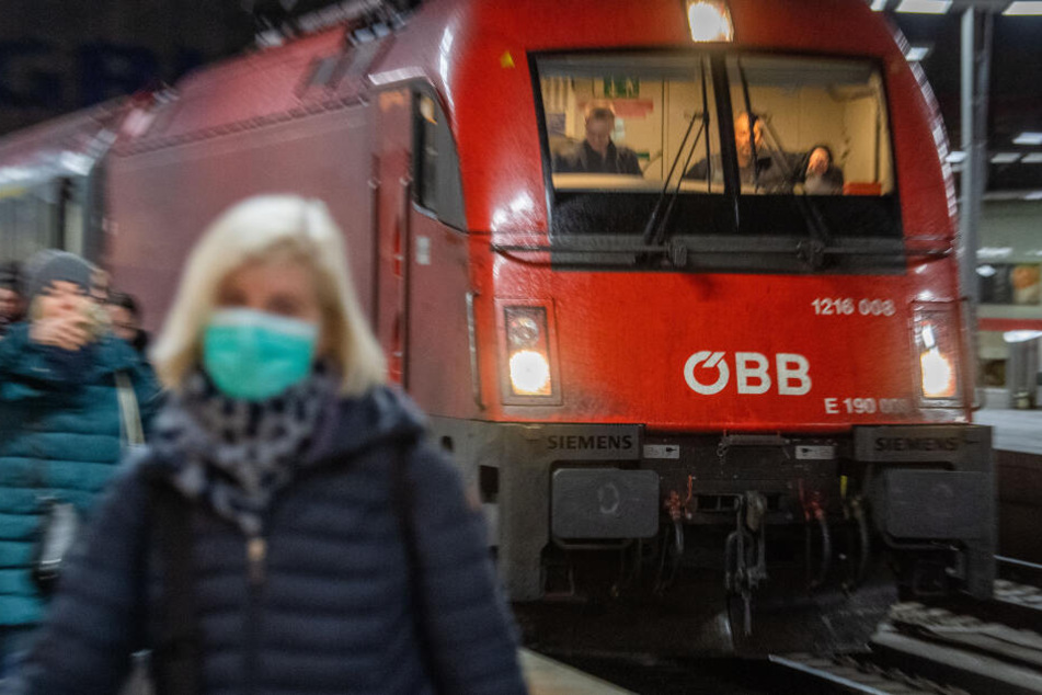 Eine Frau mit Atemschutzmaske geht vor dem Eurocity-Zug am Hauptbahnhof in München entlang.