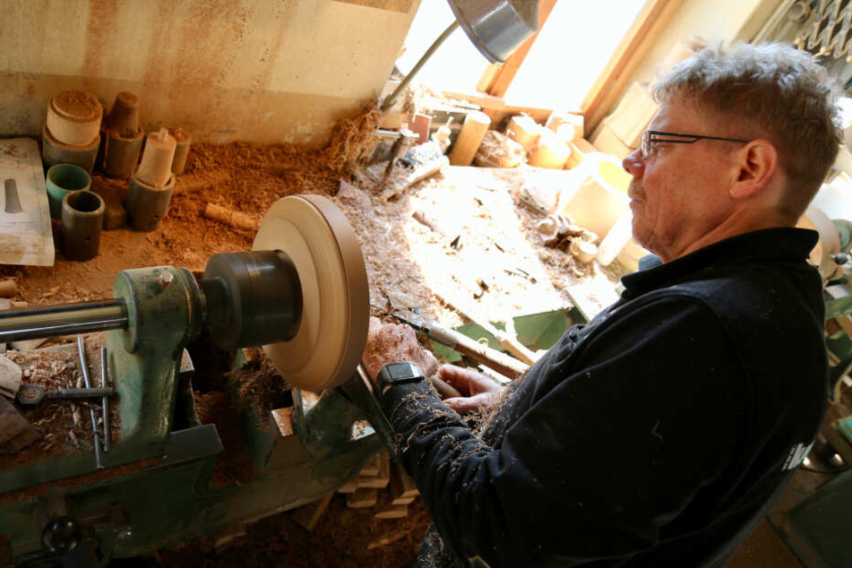 Drechslermeister Jens König steht in seiner Werkstatt an einer Drehbank und fertigt einen Schmuckteller aus Nussbaum, in dem Halsketten oder Armbänder präsentiert werden.