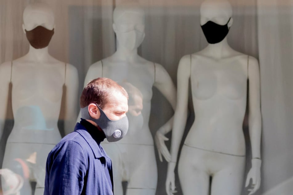 Ein Mann mit Schutzmaske läuft in Berlin-Mitte vor einem Schaufenster der "RAU Berlin Boutique" mit Schaufensterpuppen, die Stoffmasken tragen.