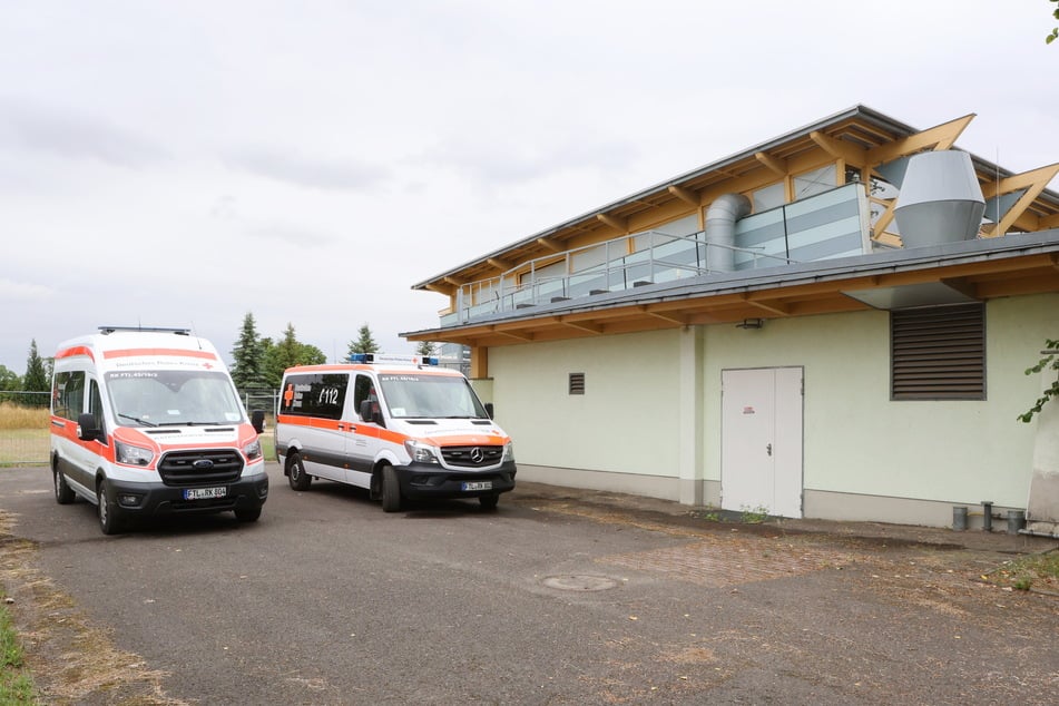 Hinter der Mehrzweckhalle in Röderau, die Notunterkunft des DRK für Einwohner aus Neudorf, parken Rettungswagen.