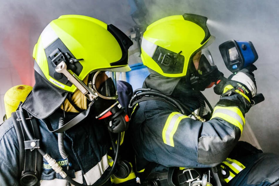 Zwei Mitglieder der Freiwilligen Feuerwehr untersuchen mit einer Wärmebildkamera bei einer Übung in Schleswig-Holstein eine verqualmte Halle.