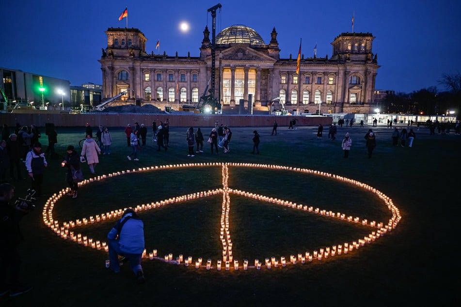 Auf einer Demonstration vor dem Reichstagsgebäude in Berlin bauen Menschen mit Kerzen im Gedenken an die Opfer des Krieges in der Ukraine ein Peace-Zeichen.