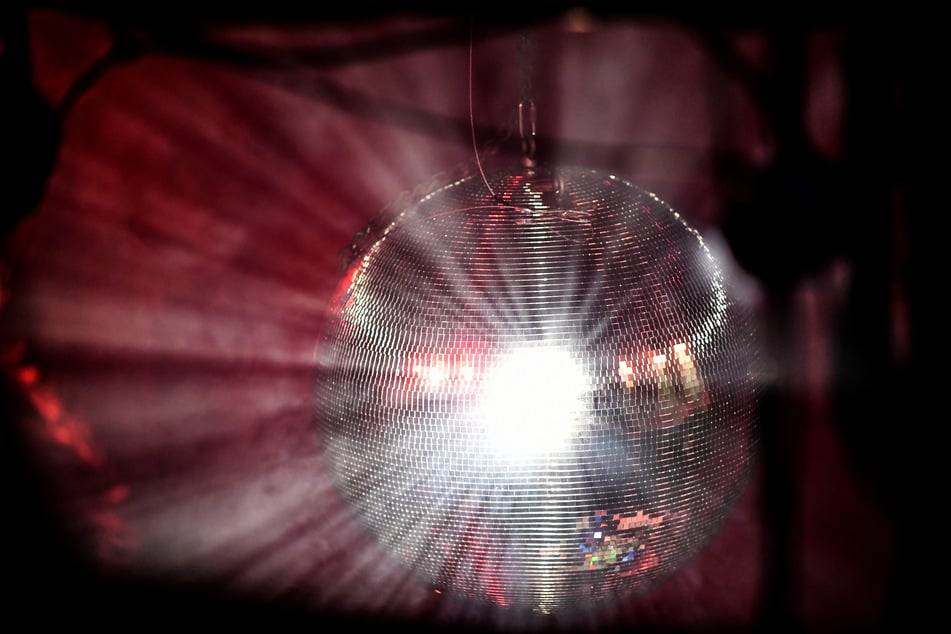 Eine Diskokugel dreht sich in einem Club und reflektiert das einfallende Licht der Scheinwerfer und Lampen.