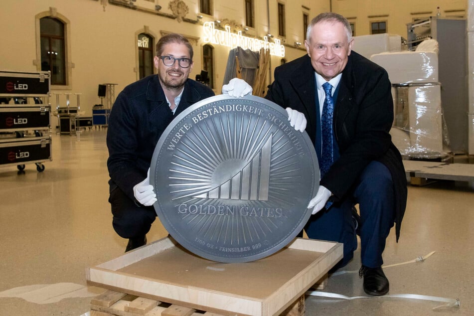 Herbert Behr (68, r.) und sein Sohn Constantin Behr (38) zeigen im Albertinum die XXL-Medaille zum Firmenjubiläum der "Golden Gates Edelmetalle".