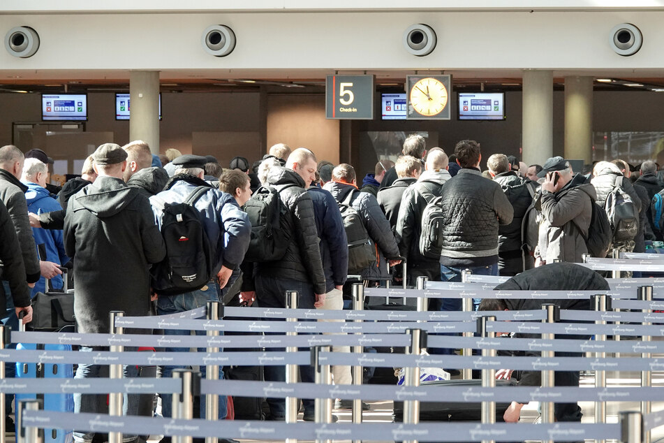 Menschen stehen an einem Check-In-Schalter für einen Flug nach Vilnius (Litauen) neben- und hintereinander. 