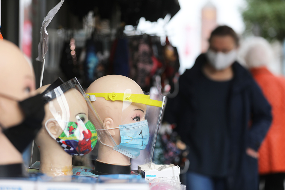 Passanten gehen an einem Geschäft vorbei, das Masken und Gesichtsschilder verkauft.