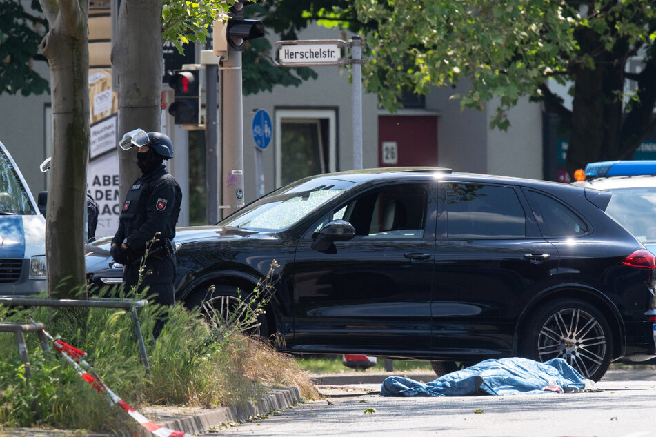 Polizisten sichern einen Tatort an der Herschelstraße, wo neben einem Auto eine abgedeckte Person liegt.