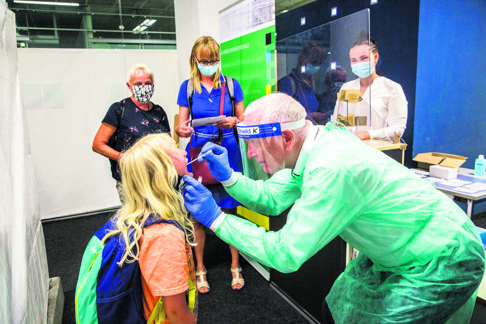 Während Dr. Klaus Heckemann (64) bei Irene (7) einen Abstrich nimmt, warten ihre Mutti und Oma im Hintergrund auf ihren Test. Ärztin Julia Heckemann (24) kennzeichnet die Teströhrchen anschließend mit einem Barcode.