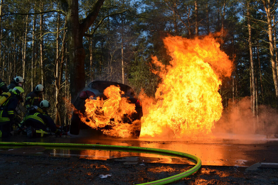 Die Wehren löschen den Opel Astra. Der Wagen fing nach einer Kollision mit einem Baum Feuer.
