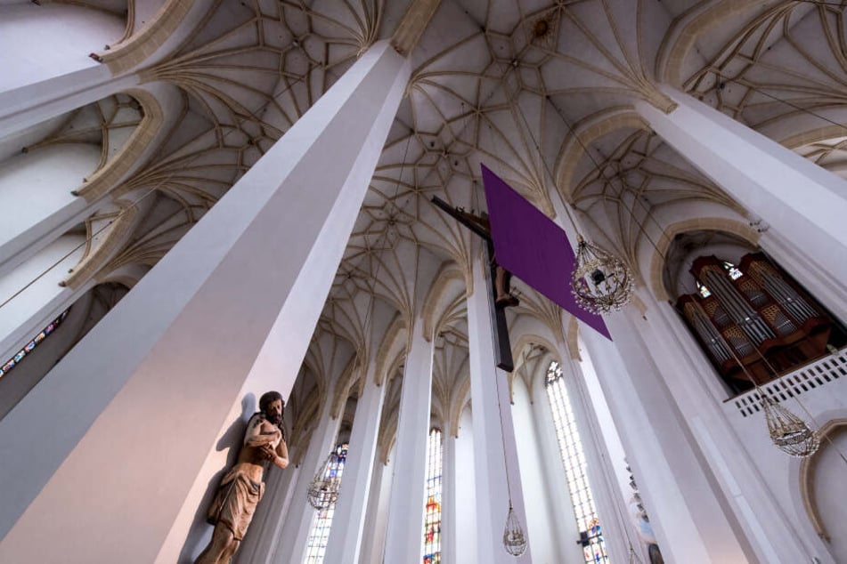 Ein lila Tuch verhüllt in der Frauenkirche ein Kreuz. In vielen Kirchen werden Darstellungen von Jesus in der Zeit vor Ostern verhüllt.