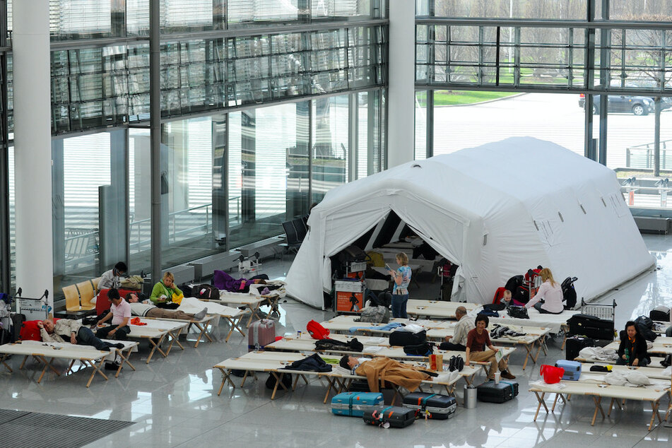 Fluggäste sitzen am am Flughafen auf Feldbetten in einer Notunterkunft im Terminal 2.