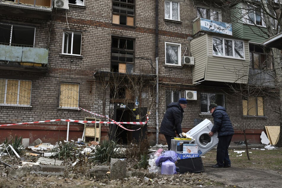 Anwohner tragen eine Waschmaschine beim Verlassen ihres Hauses in Saporischschja, das bei einem nächtlichen Raketenangriff beschädigt wurde.