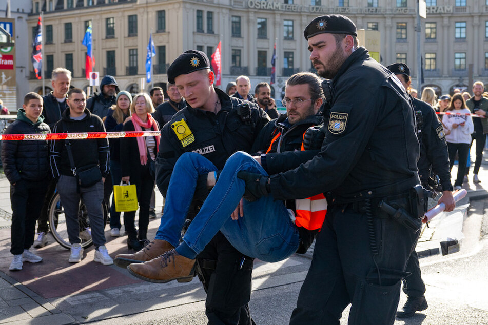 Polizisten tragen einen Klimaaktivisten weg, der sich zuvor am Karlsplatz auf die Straße geklebt hatte.