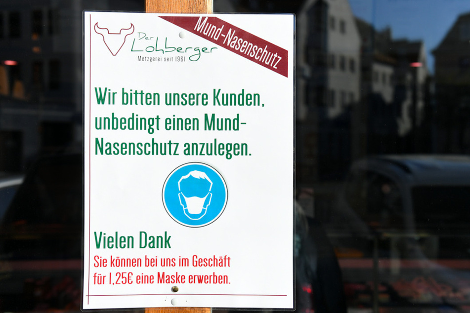An der Tür einer Metzgerei wird über einen Aushang auf die Maskenpflicht hingewiesen.