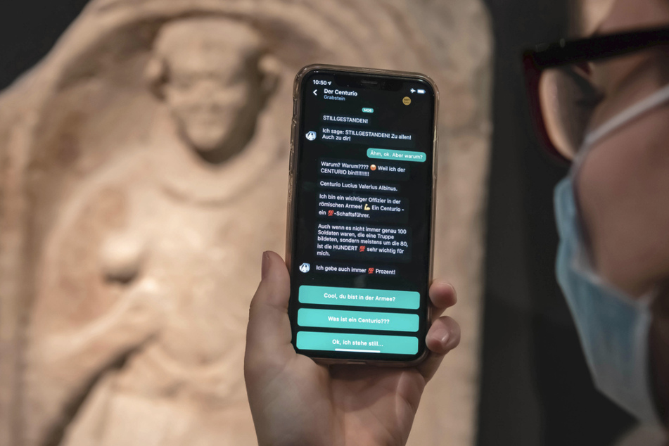 Im Badischen Landesmuseum wird vor einem Grabstein eines Centurio aus dem 1. Jahrhundert nach Christus auf einem Smartphone eine App gezeigt, mit der Museumsbesucher Kontakt zu Ausstellungsobjekten aufbauen können.