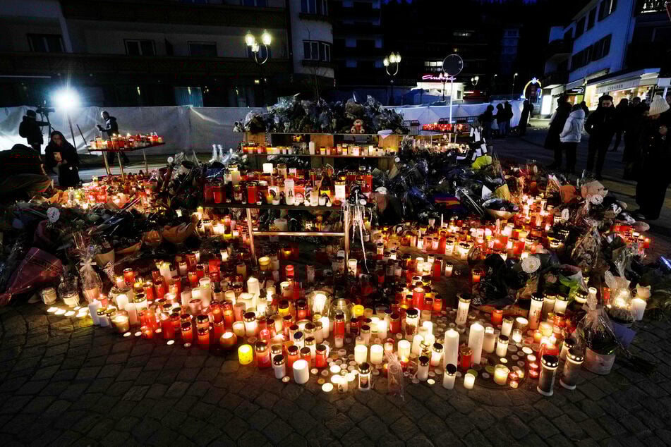 Menschen zünden Kerzen an und legen Blumen vor der versiegelten Bar Le Constellation in Crans-Montana.
