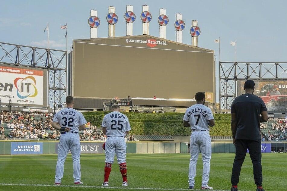 Gavin Sheets, Andrew Vaughn, and Tim Anderson of the Chicago White Sox bow their heads in a moment of silence for the victims of the mass shooting in Highland Park, Illinois.