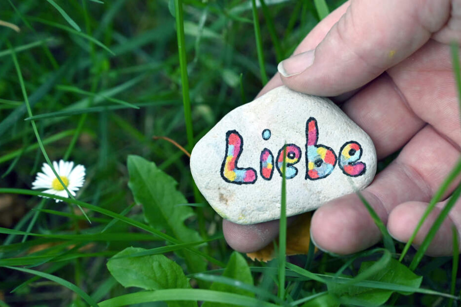 Ein Stein mit der Aufschrift "Liebe" wird ins Gras gelegt.