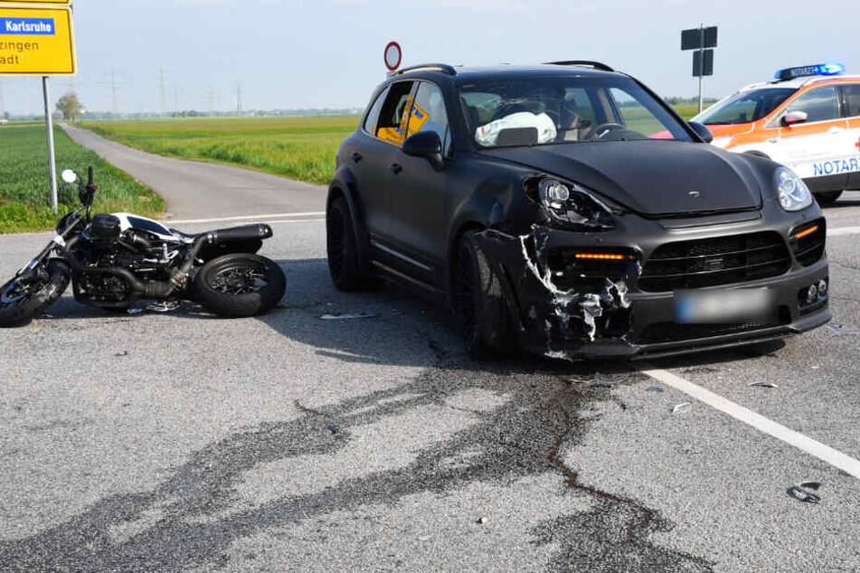 Ein Notarzt an der Unfallstelle, neben dem Motorrad und verunfallten Porsche.