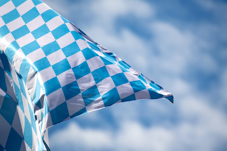 Die bayerische Flagge mit weiß-blauen Rauten weht vor weiß-blauem Himmel im Wind. (Symbolbild)