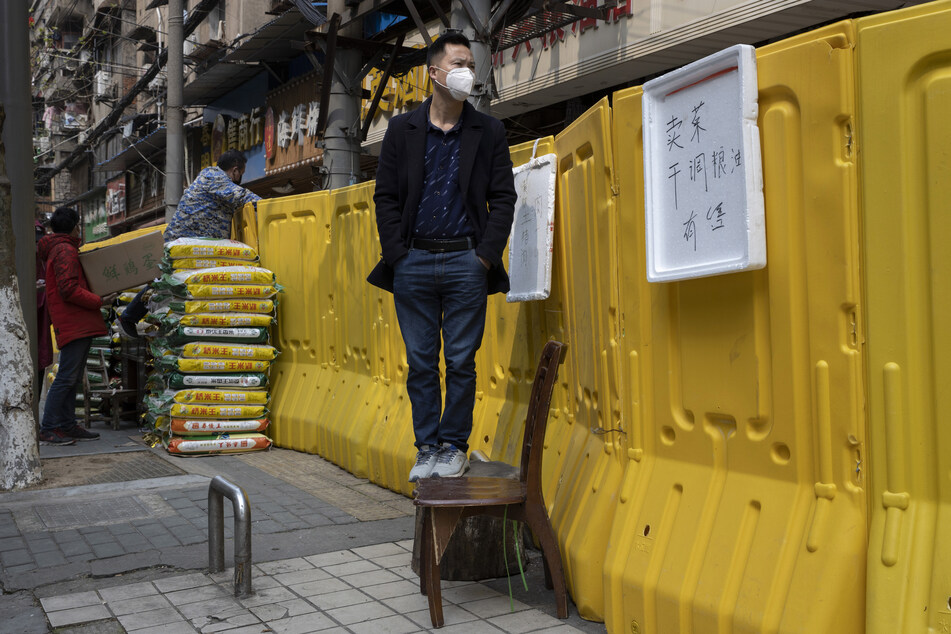 Ein Anwohner mit Mundschutz steht auf einem Stuhl, um über Barrikaden zu sehen, mit welchen ein Stadtteil in Wuhan abgeriegelt wurde.