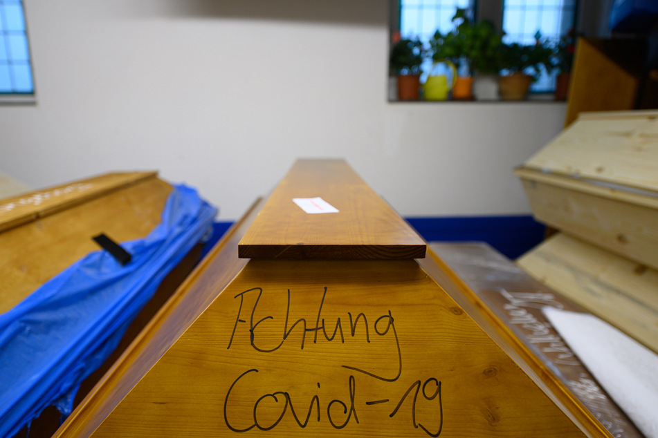 "Achtung Covid-19" steht auf einem Sarg mit einem Verstorbenen, der an oder mit dem Coronavirus gestorben ist, welcher im Krematorium in der Kühlung steht.