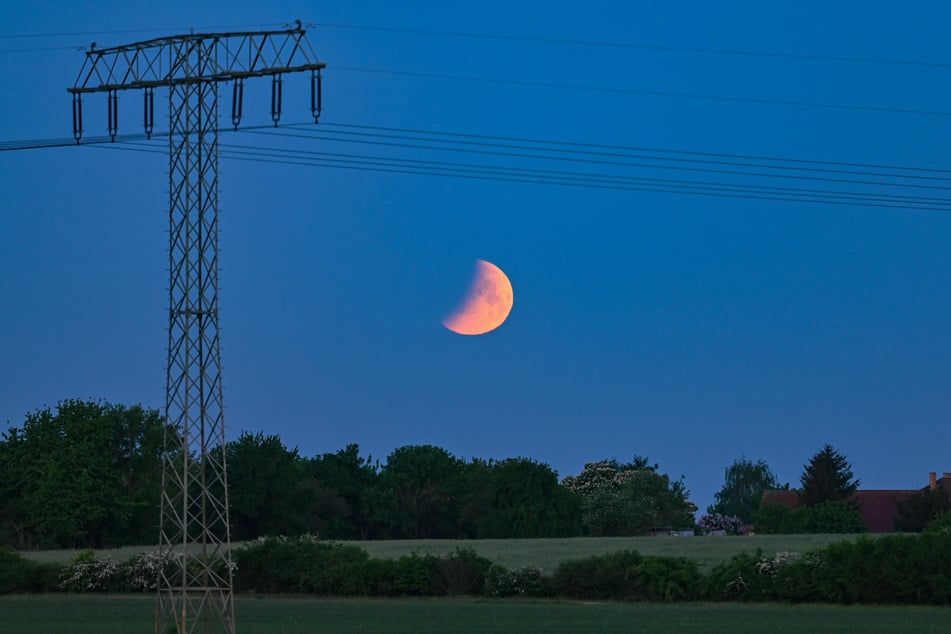 Der Beginn der Mondfinsternis ist am frühen Morgen über der Landschaft neben einem Hochspannungsmast im brandenburgischen Jacobsdorf zu sehen.