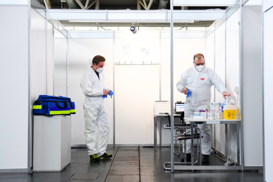 Ein Arzt und ein Mitarbeiter des Rettungsdienstes ziehen bei einem Pressetermin im neu eingerichteten Impfzentrum in der Messe München in einer Impfkabine Schutzkleidung an.