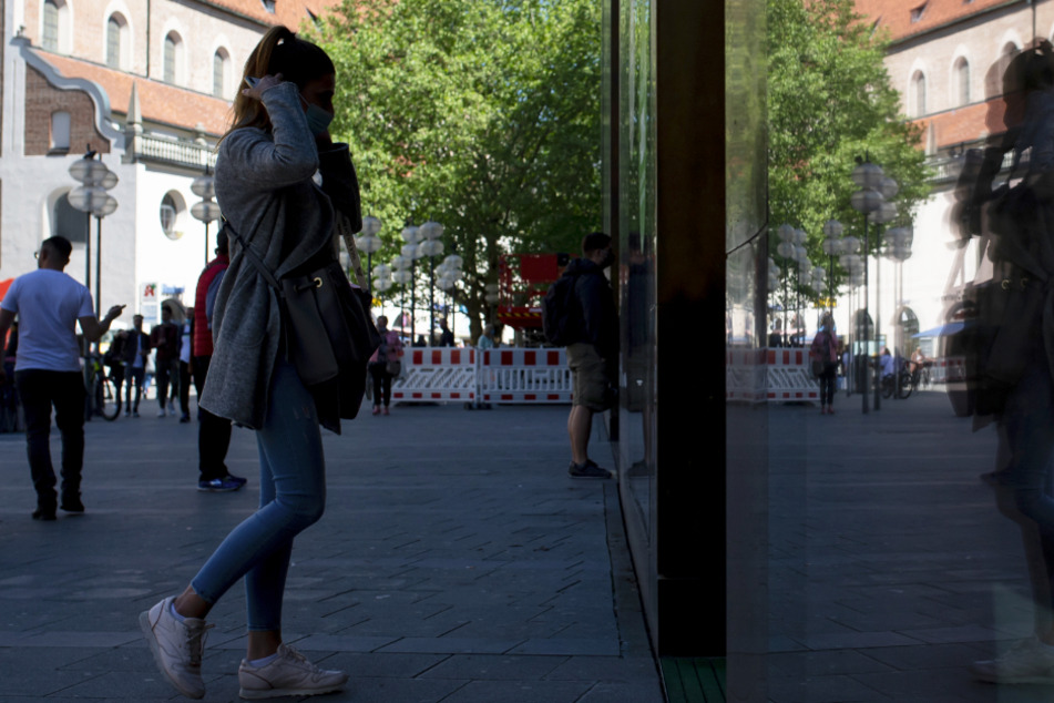 Passanten betreten in der Fußgängerzone in der Innenstadt ein Geschäft und spiegeln sich dabei in einer Fensterscheibe.