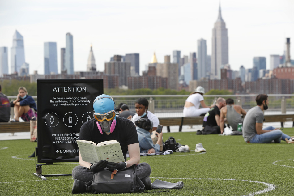 New York: Ein Mann trägt eine Schutzbrille und eine Schutzmaske, während er im Domino Park im Stadtteil Brooklyn und ein Buch liest.