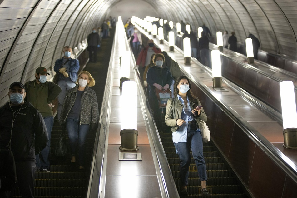 Menschen, die zum Schutz vor Coronaviren Gesichtsmasken und Handschuhe tragen, halten sich fast alle an die Richtlinien zur sozialen Distanzierung, während sie auf der Rolltreppe zur U-Bahn hinuntergehen.
