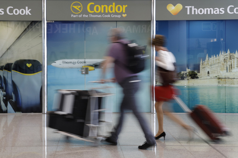 Passagiere gehen an einem Büro von Condor und Thomas Cook am Flughafen Palma de Mallorca vorbei. (Symbolfoto)