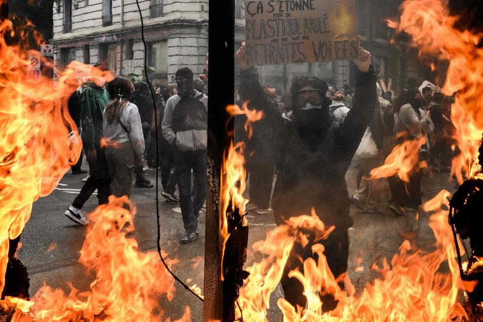 Ein Protestierender in Lyon hält ein Schild hoch mit der Aufschrift: "Von verbranntem Plastik erschüttert, aber nicht von unseren gestohlenen Renten."