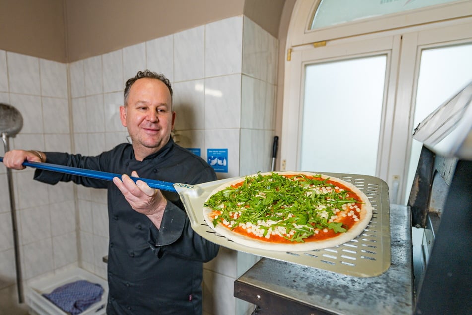 Papa Xheki (50) schiebt eine Pizza in den Ofen.