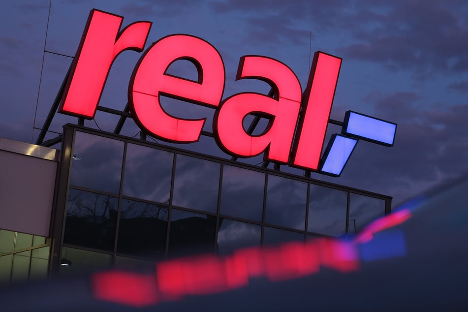 Das Logo leuchtet am Morgen auf dem Dach eines Real Supermarktes. (Symbolbild)