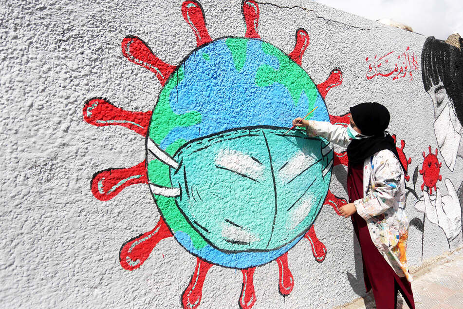 Eine Frau malt eine Coronavirus-Erde an eine Graffiti-Wand.