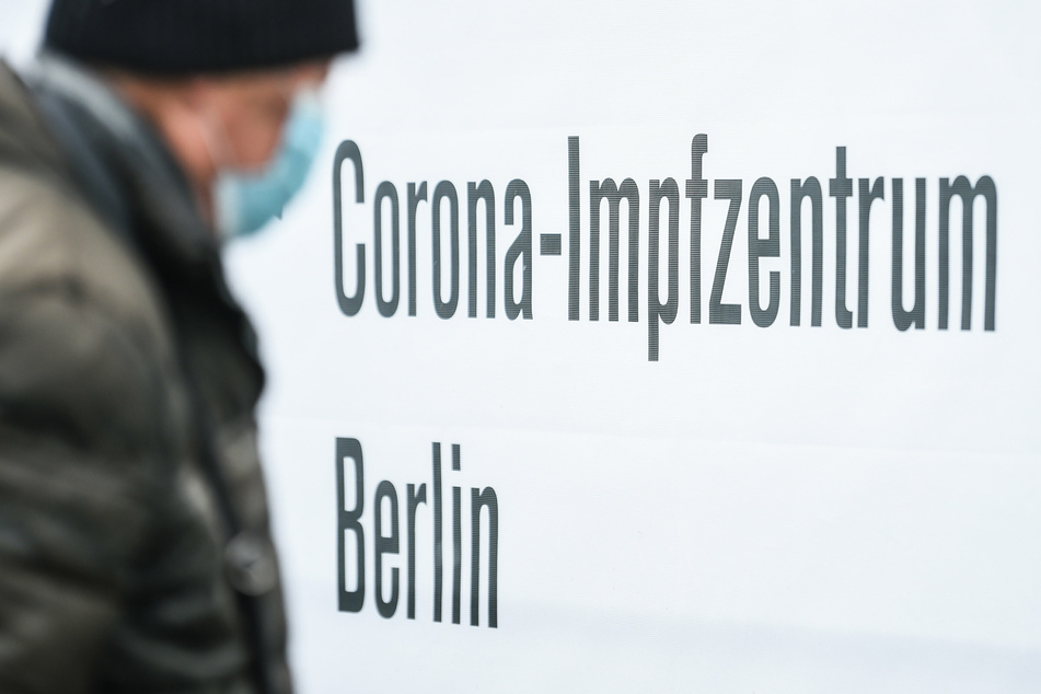 Eine Person mit Mund-Nasen-Bedeckung geht an einem Schild mit der Aufschrift "Corona-Impfzentrum Berlin" vorbei.