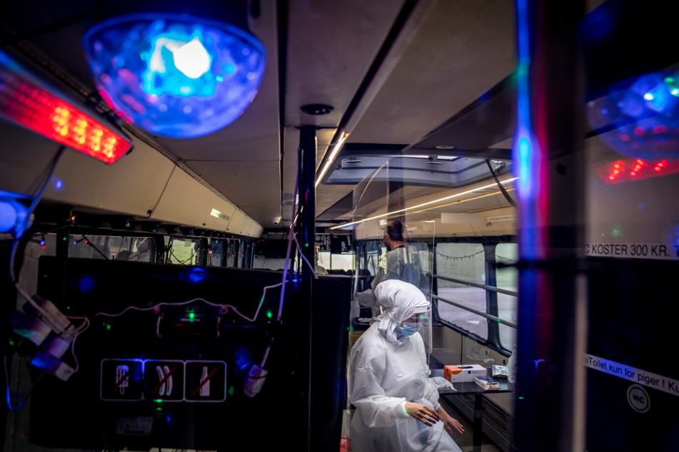 Dänemark, Ishoej: Eine Frau in Schutzausrüstung sitzt in einer mobilen Corona-Teststation in einem Bus. Disco-Beleuchtung und Musik sollen den Besuchern im Bus die Zeit angenehmer gestalten, während sie getestet werden.