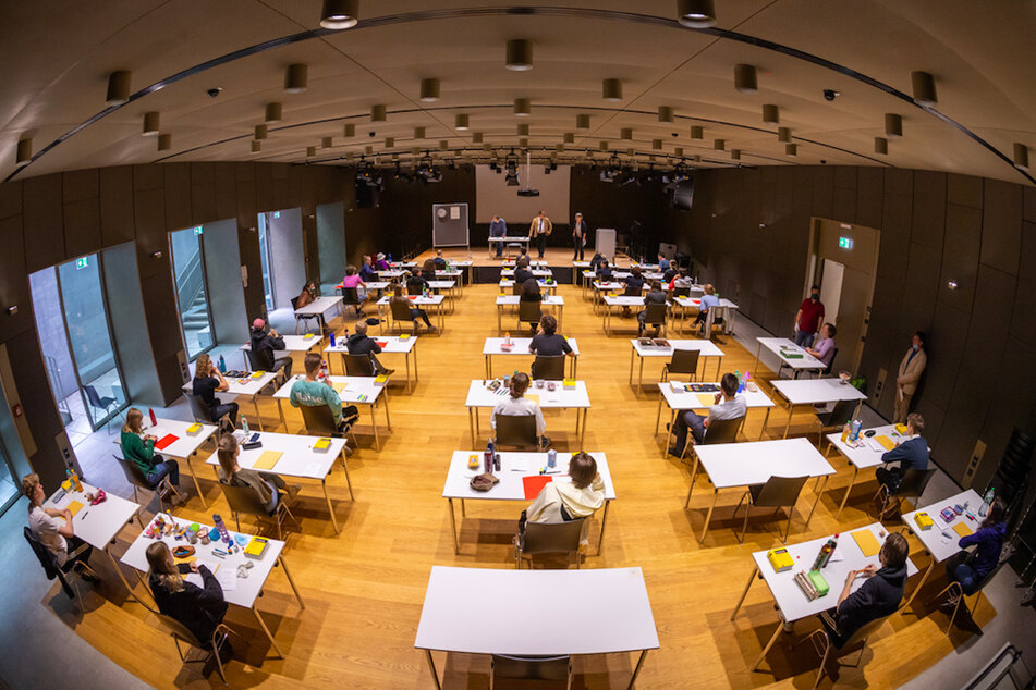 Mit weitem Abstand sitzen Schüler zur Abiturprüfung in Deutsch an ihren Tischen in der Schulaula.