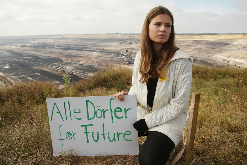 Die Umweltaktivistin Luisa Neubauer sitzt mit einem Plakat mit der Aufschrift "Alle Dörfer For Future" vor dem Garzweiler Tagebau.