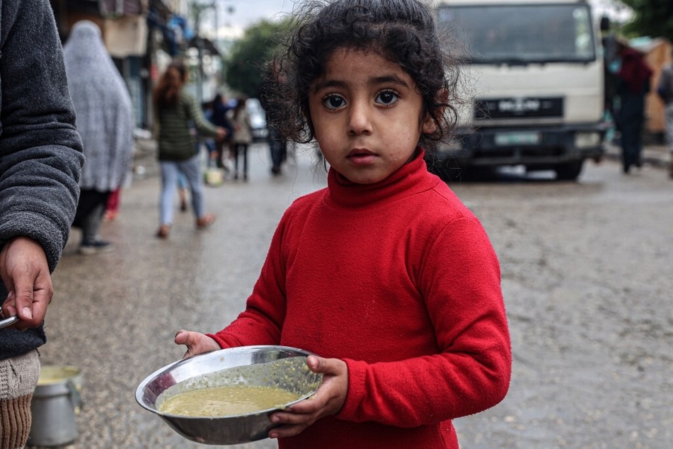 A displaced Palestinian girl carries a ration of red lentil soup, distributed by volunteers in Rafah in the southern Gaza Strip.