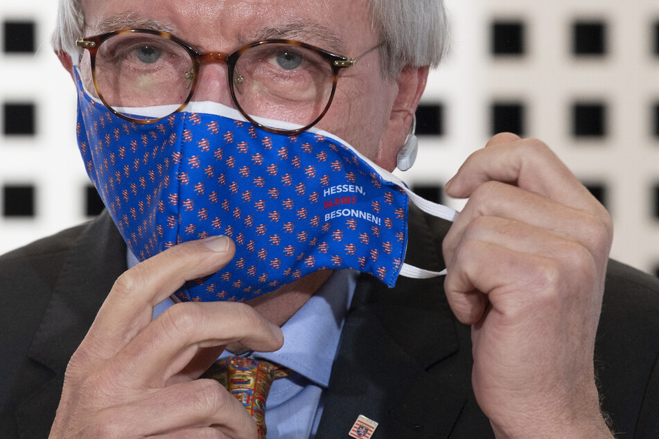 Der hessische Ministerpräsident Volker Bouffier (CDU) hantiert mit seiner Mund-Nasen-Bedeckung.