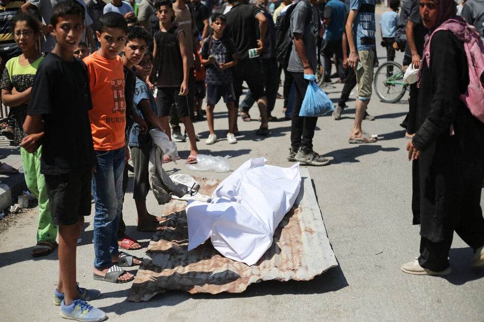 People surround the body of a Palestinian woman who was shot while seeking aid at a Gaza Humanitarian Foundation distribution point, at the entrance of the Bureij refugee camp in the central Gaza Strip on July 27, 2025.