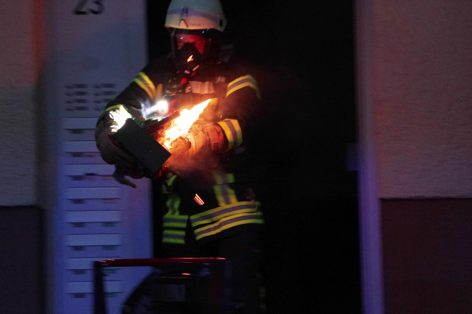 Unter schwerem Atemschutz und mit feuerfester Kleidung trug ein Feuerwehrmann den mutmaßlichen Brandherd ins Freie.