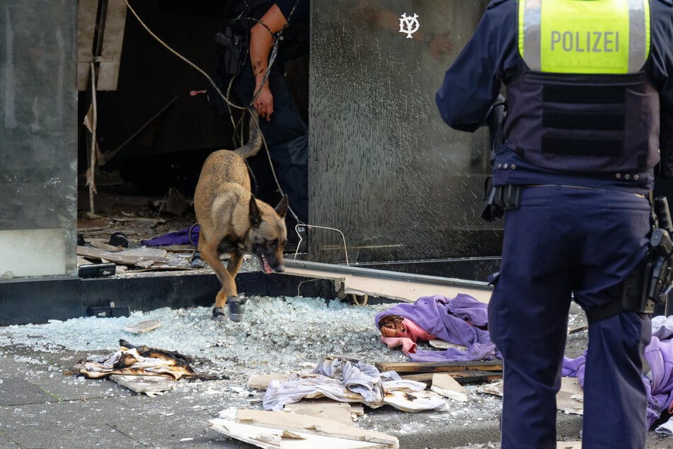 Ein Polizeihund sucht in den Trümmern des betroffenen Ladenlokals nach Spuren.