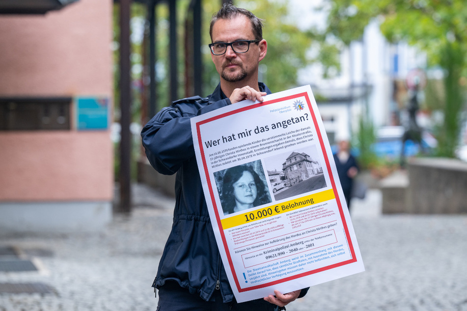 Ein Polizeibeamter hält das neue Plakat zum Zeugenaufruf im Mordfall Christa Mirthes.