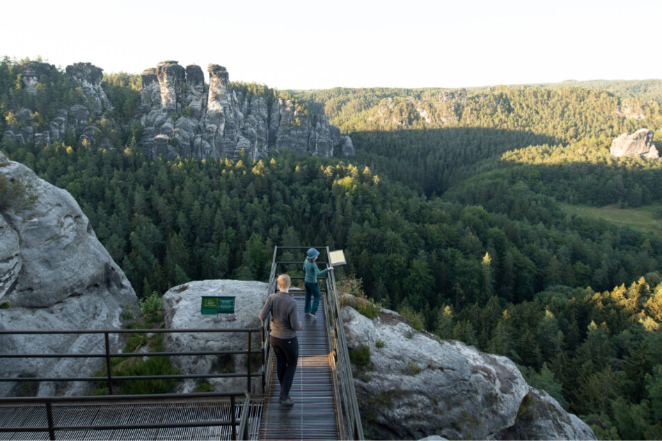 Touristen stehen im Nationalpark Sächsische Schweiz in der Felsenburg Neurathen auf einer Aussichtsplattform.
