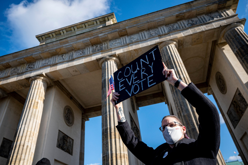 Eine Teilnehmerin auf der Kundgebung unter dem Motto "Friedlicher Übergang der Präsidentschaft und eine demokratische USA" hält vor dem Brandenburger Tor in Berlin ein Schild mit der Aufschrift "Count Every Vote" und eine Mini-US-Flagge hoch.