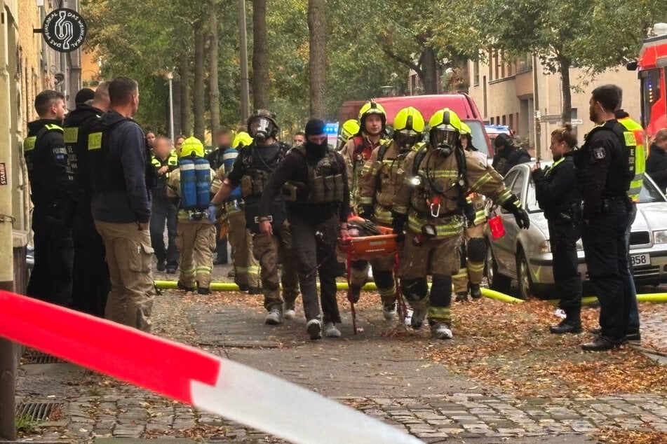 Die Einsatzkräfte tragen eine leblose Person in Freie, die aus der brennenden Wohnung geborgen worden ist.